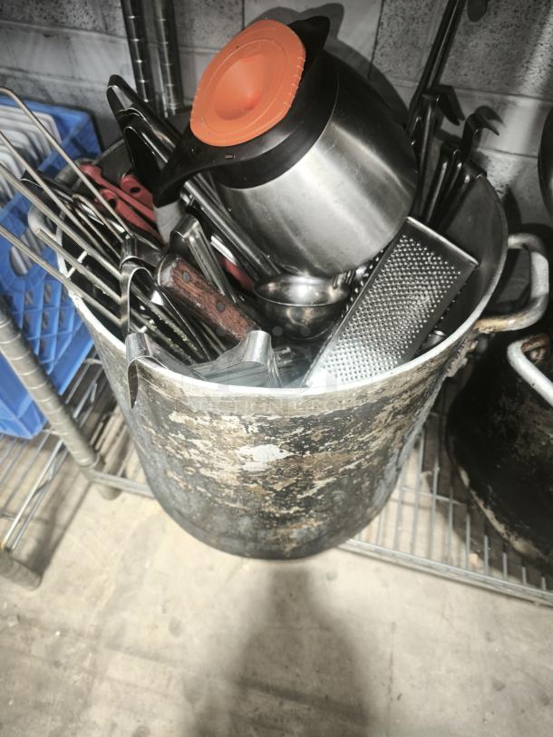 Old metal pan filled with assorted kitchen tools, including a grater and a jug with an orange lid. Pan shows signs of wear.