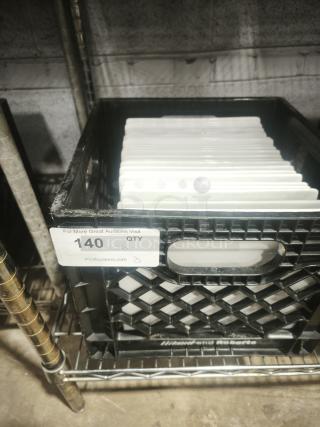 9" bright white square porcelain plates stacked in a crate, quantity 26 label visible, stored on a metal shelf.
