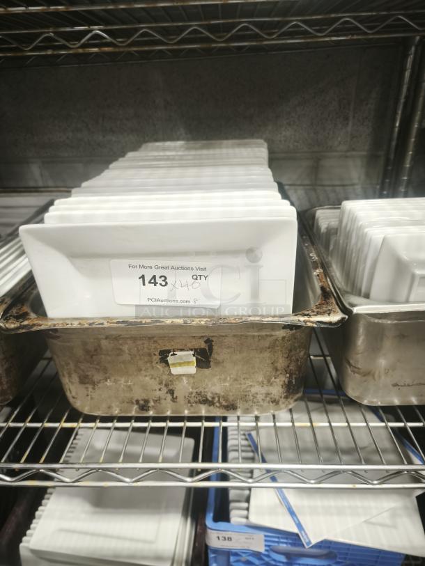 9" bright white square porcelain plates, stacked in storage. Auction tag indicates quantity of 143.