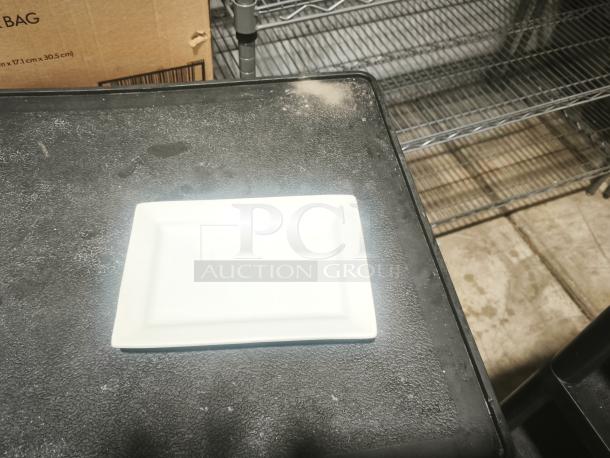 Rectangular bright white porcelain plate with a smooth surface, shown on a textured black surface. Ideal for serving.