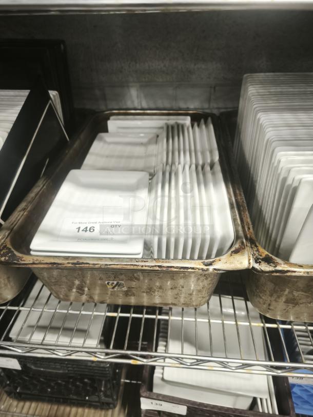 Bright white square porcelain plates stacked in a metal tray. Auction label shows quantity of 146. Plates appear in good condition.