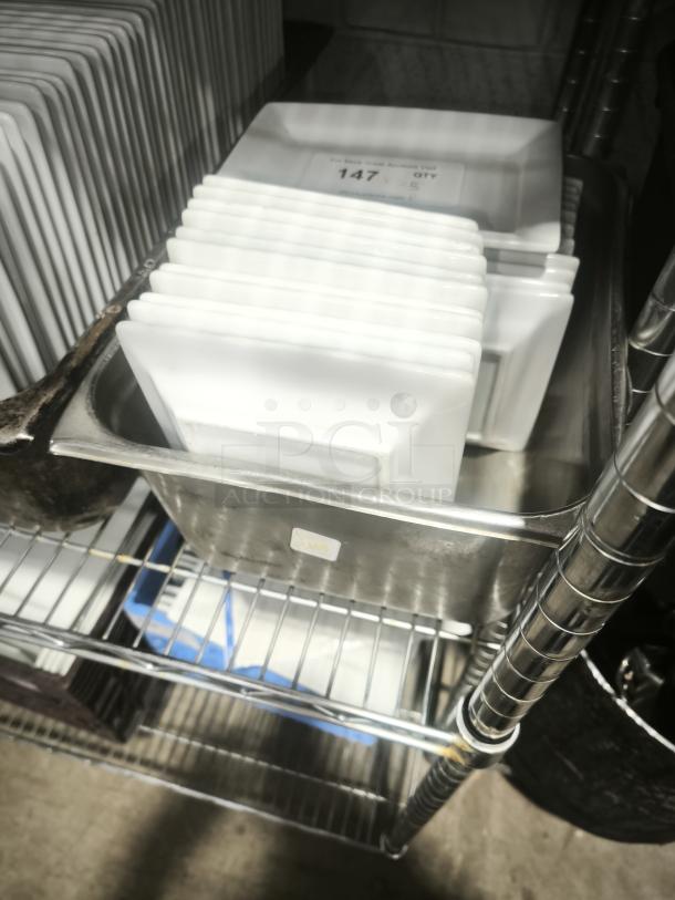 Rectangular bright white porcelain plates stacked on a metal shelf. Label indicates quantity: 147. Excellent condition.
