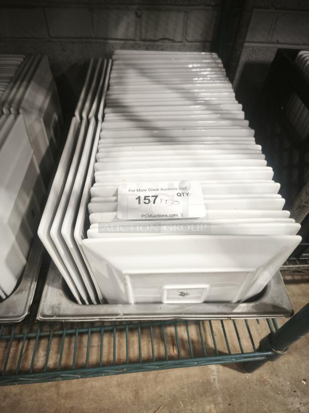 9" bright white square porcelain plates stacked in a metal bin, totaling 157 in quantity, glossy finish, unused condition.