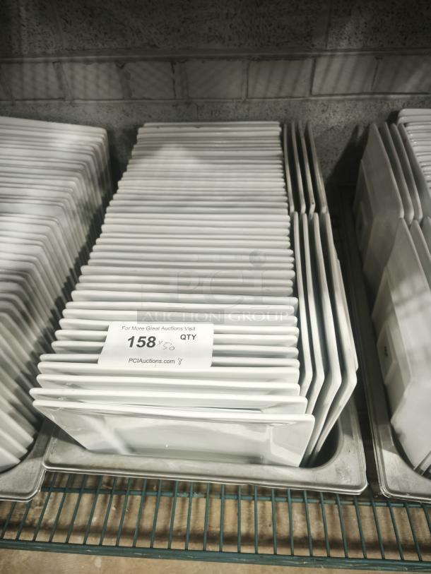 Stack of 9" bright white square porcelain plates, new condition, labeled "158 QTY" on a metal shelf for auction.