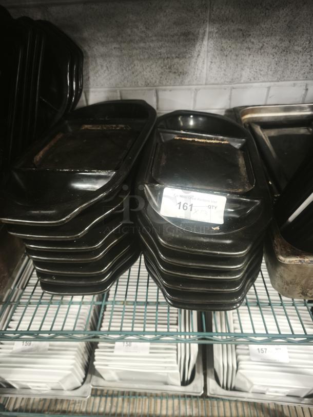 Stack of iron griddle pans on a shelf, showing signs of use. A label with "161" is partially visible on one pan.