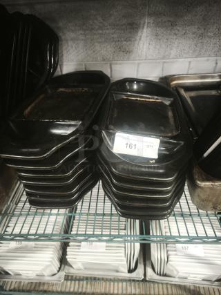 Stack of iron griddle pans on a shelf, showing signs of use. A label with "161" is partially visible on one pan.