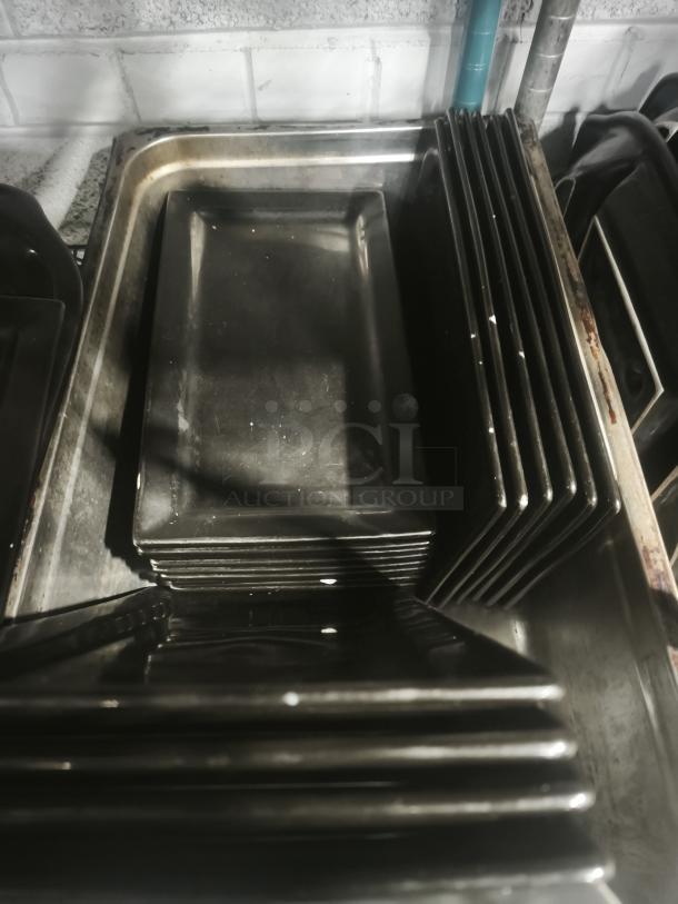 6"x8" rectangular black porcelain plates stacked, showing slight wear. Ideal for serving, smooth glossy finish.