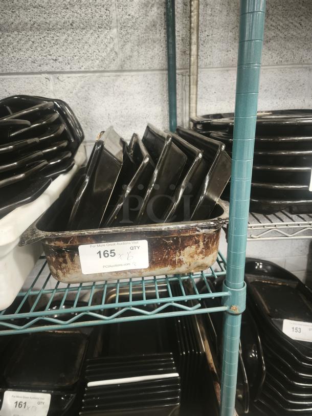 Black rock hot stone serving platters stacked on a metal shelf. Includes worn labels indicating PCI Auctions and quantity.