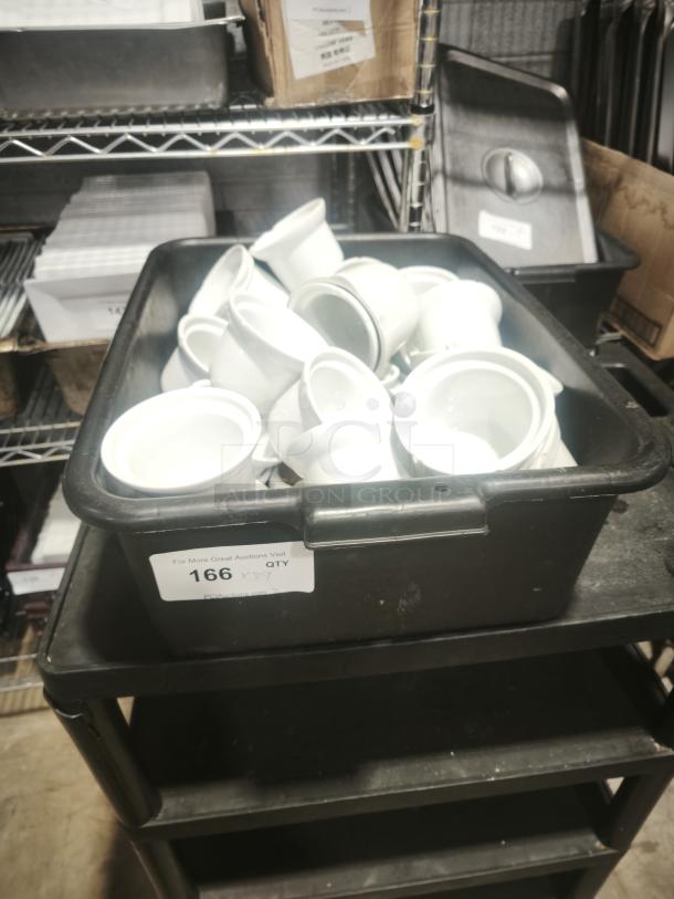 White porcelain pot pie dishes stacked in a black container, labeled "166 X QTY," on a shelf in storage.
