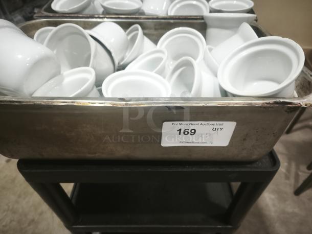 White porcelain pot pie dishes stacked in a metal container, labeled with "169 QTY 29" indicating quantity.