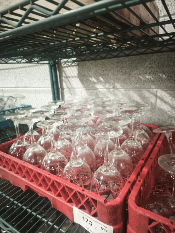 A set of wine glasses stored upside down in a red rack, on a metal shelf. Visible label reads "173".