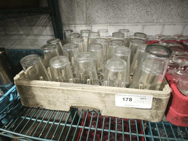 Vintage glass tumblers in a crate, quantity 24, displayed on metal shelves. Ideal for restaurant use.
