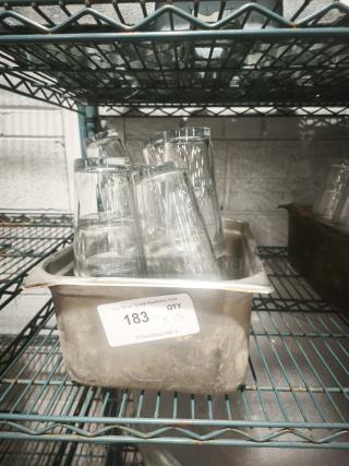 Vintage glass tumblers in a metal container on a shelf, labeled "183 QTY x15," showcasing clear glass detailing.