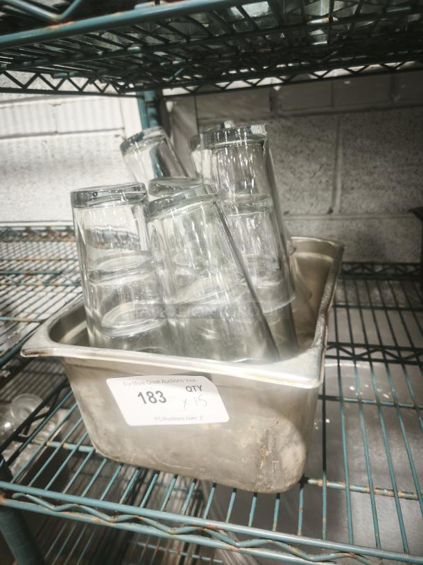 Vintage glass tumblers in a container on a metal shelf. Set of 15, good condition. Auction number 183 label visible.