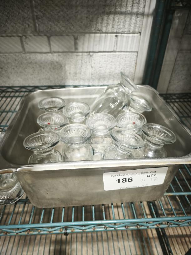 Set of clear glass footed items, 6" tall, in a metal container. Includes twelve pieces, in excellent condition. Auction lot 186.