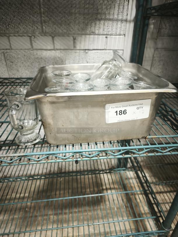 Clear glass footed mugs, 6" tall, set of 12, in good condition. Placed in a metal tray with auction lot tag "186".