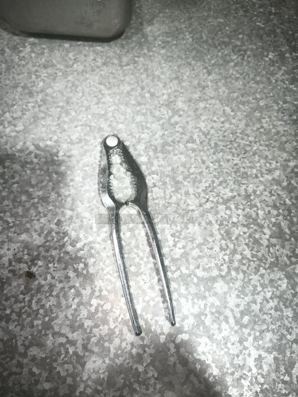 Stainless steel crab cracker tool on a textured surface, used for cracking crab legs. Appears in good condition.