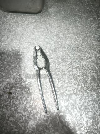 Stainless steel crab cracker tool on a textured surface, used for cracking crab legs. Appears in good condition.