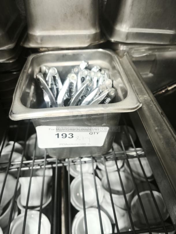 Stainless steel crab crackers and tools set in a metal container, labeled for auction, suitable for seafood kitchen use.