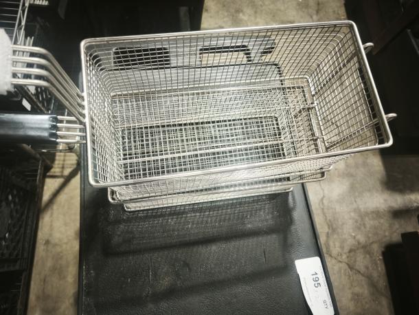 Brand new commercial wired mesh fry basket with front hook and black non-slip grip handle, placed on a black surface.
