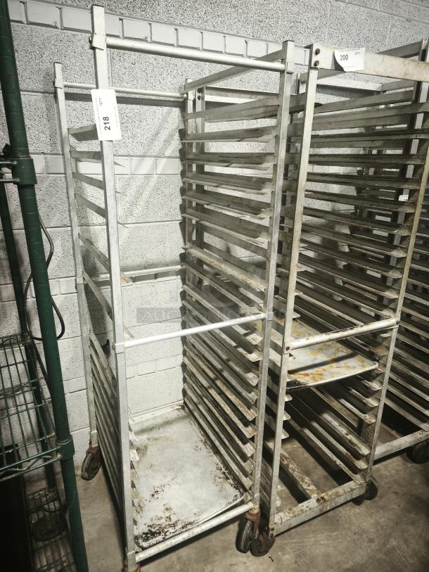Aluminum bakers rack with multiple shelves, used condition, on wheels, visible lot tags with numbers 218 and 200.