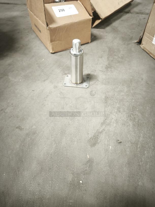 Brand new stainless steel leg assembly with square mounting plate, shown on warehouse floor near cardboard boxes marked "298 QTY."