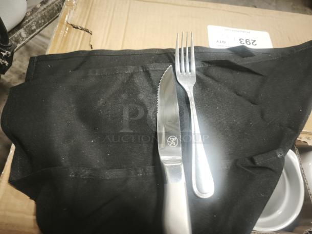 Brand new silverware set with fork and knife on black towel, placed on a cardboard box. Knife features a logo.
