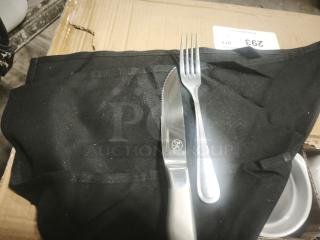 Brand new silverware set with fork and knife on black towel, placed on a cardboard box. Knife features a logo.
