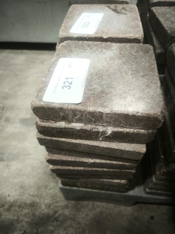 Stack of NSF certified volcanic granite slabs for cooking, showing light surface wear and auction lot labels.