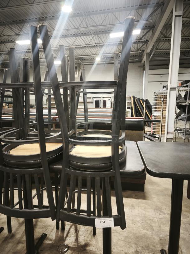 Black metal channel back bar stool with black vinyl seat, stacked upside down. Features a modern design and sturdy construction.