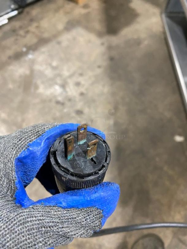 Close-up of a power plug for Precision SST2024RTNYC refrigerated food bar, with textured gloves holding it over a concrete floor.