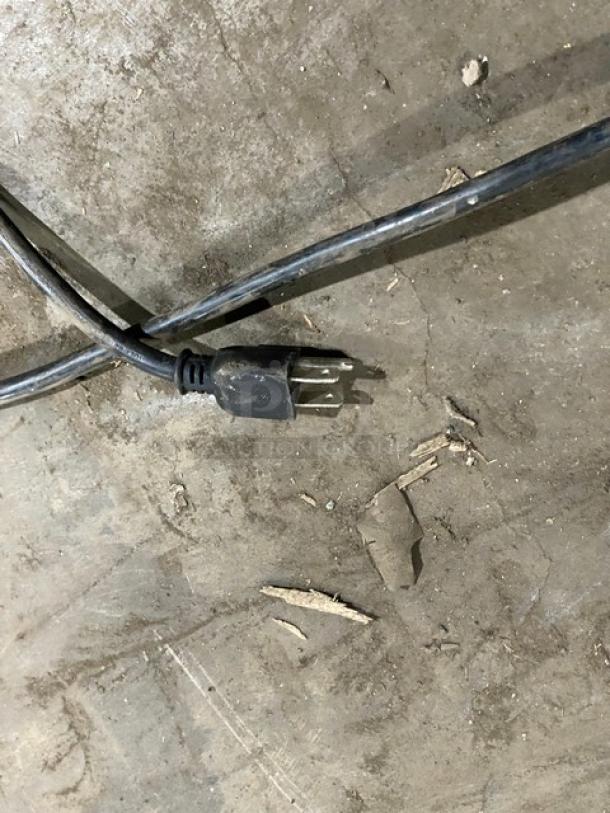 Black 3-prong electrical plug resting on a concrete floor, part of the Leader refrigerated worktop unit.