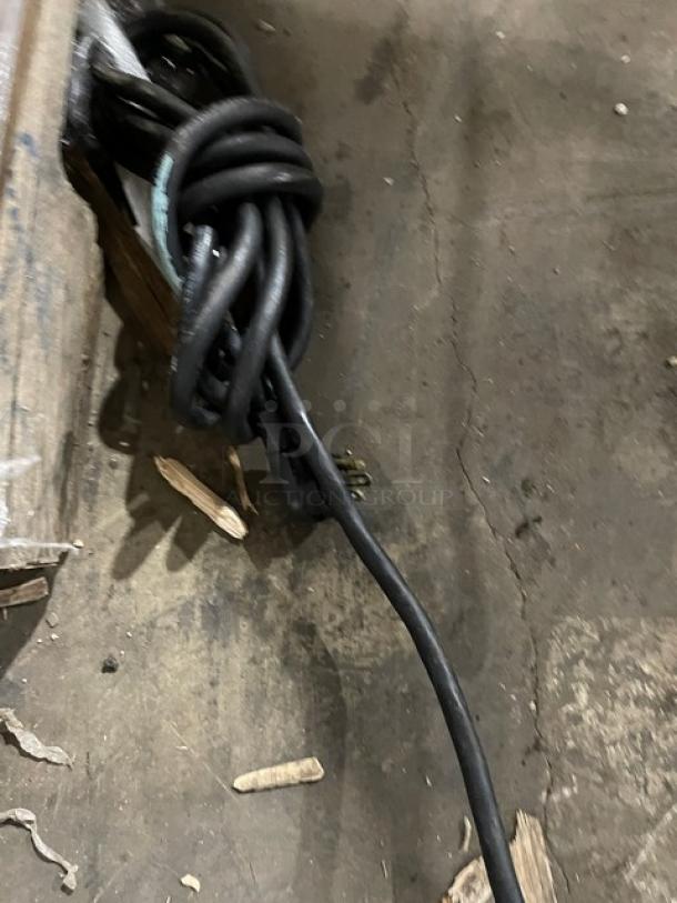A coiled black power cable for the Imbera G319 refrigerator, lying on a concrete floor near wooden debris.