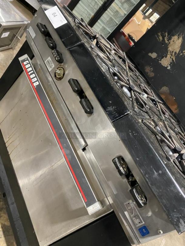 Garland commercial stainless steel gas-powered 6-burner range/oven combo with backsplash, overhead salamander shelf, and wired oven rack.