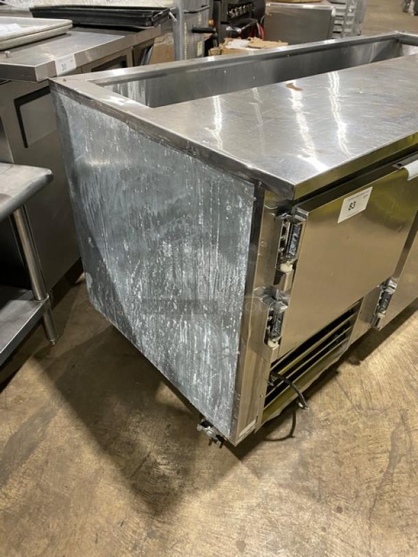 Leader 3-door stainless steel refrigerated prep table with poly coated rack, visible wear, on casters for mobility.