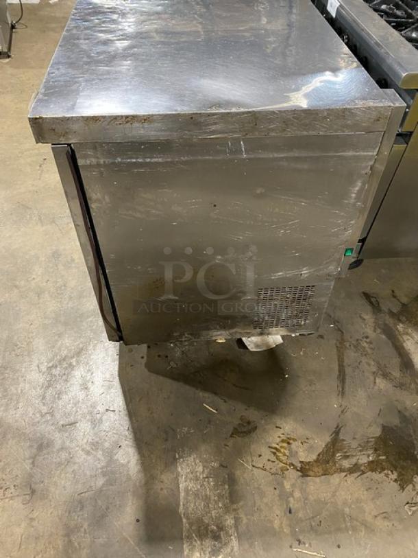 Coldline commercial stainless steel 3-door worktop refrigerator on casters, with poly-coated wire rack, showing signs of use.
