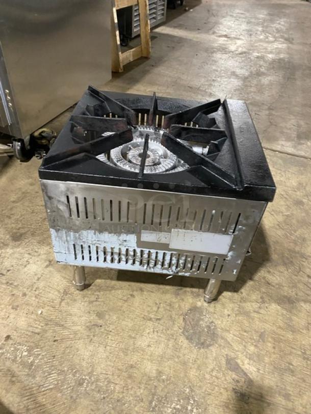 Commercial stainless steel gas-powered single burner stock pot range with legs. Visible wear, industrial kitchen setting.