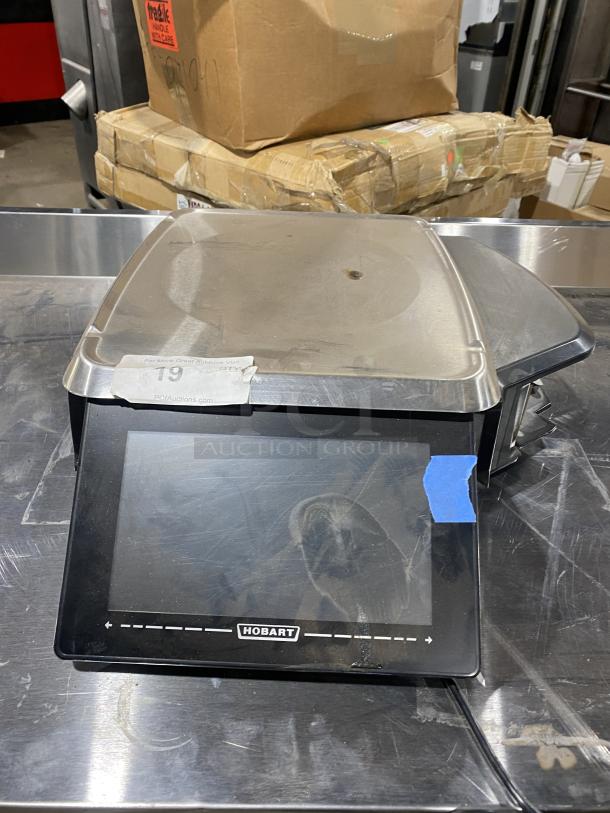 Hobart HT-Series black electric price computing scale with printer. Model HTi-7LH4. Features stainless steel worktop and dual displays.