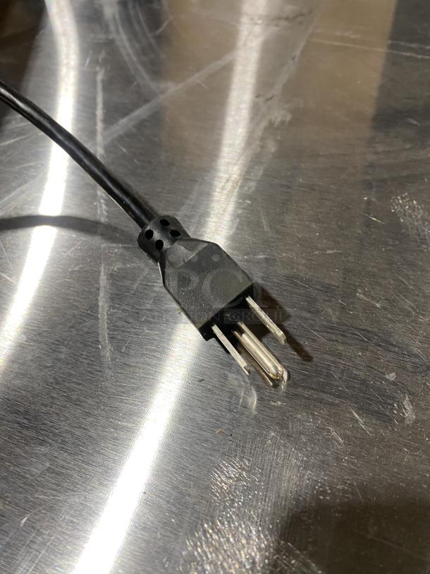 Close-up of a power plug on a stainless steel countertop background, likely part of a Hobart HT-Series commercial scale system.