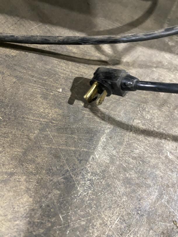 Power cord plug for True TWT-60 undercounter refrigerator on a textured surface.