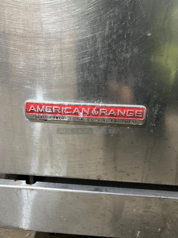 American Range commercial stainless steel 4-burner gas range/oven with backsplash, salamander shelf, and legs. Logo visible.