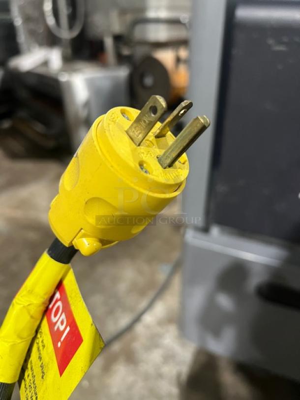 Yellow power plug for Ojeda ALPA-120 G2 refrigerated display case, 120V, with attached warning tag.
