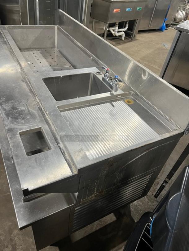 Custom stainless steel bar station with single drawer, integrated ice bin, sink, drain board, backsplash, on legs.