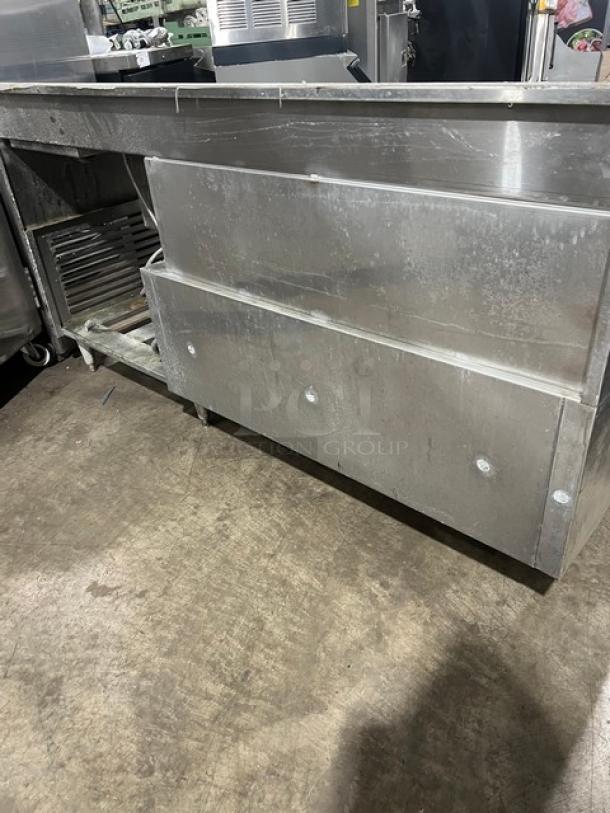 Custom stainless steel bar station with single drawer, backsplash, integrated ice bin, sink, and drain board on legs.