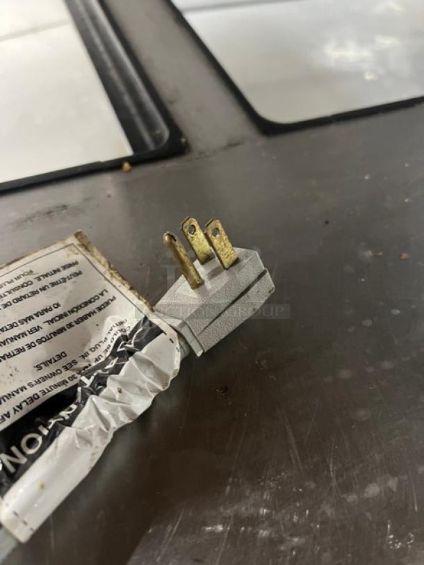 Close-up of a power plug for True TSSU-60-24M-B-ST-HC refrigerated prep table, showing three prongs and adjacent label.