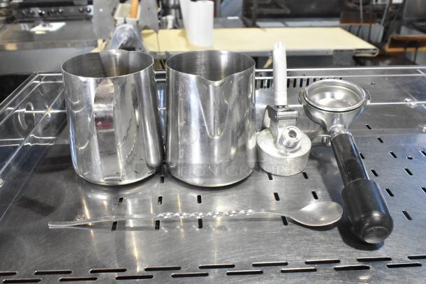 Grimac VD2GE espresso machine accessories: two milk frothing pitchers, one portafilter, steam wand, and spoon.