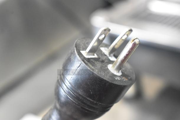Close-up of a 220V plug for a Grimac VD2GE commercial espresso machine, showcasing prongs and black casing.