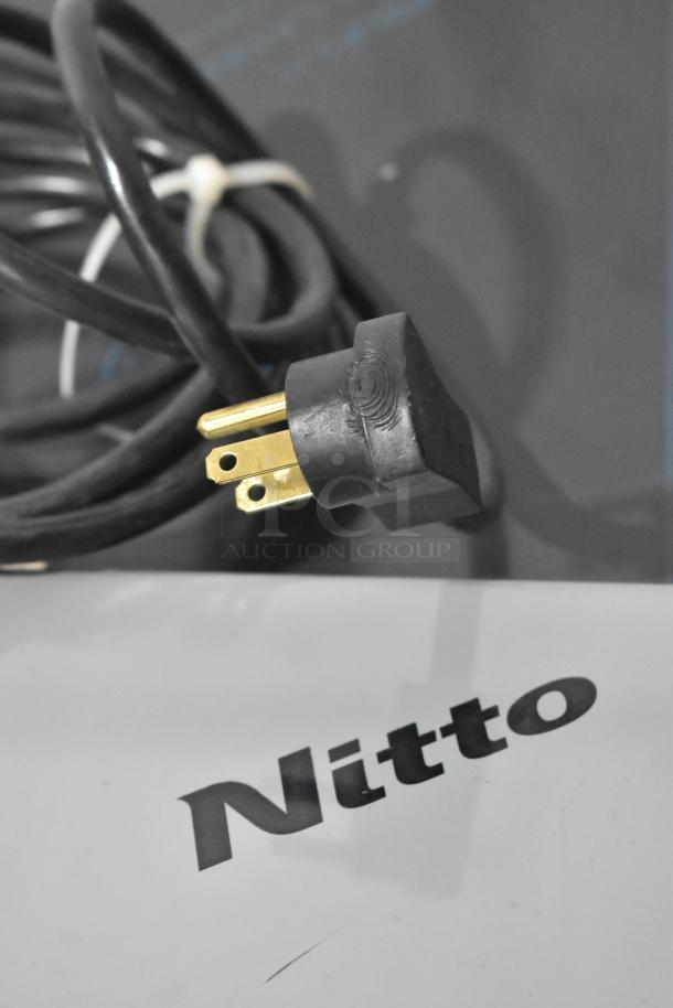 Black electrical power plug and cable on a surface with "Nitto" text. Plug has three prongs, coiled cord.