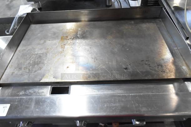Stainless steel commercial gas griddle on stand, by Standard Range. Shows wear, scratches, and some discoloration.