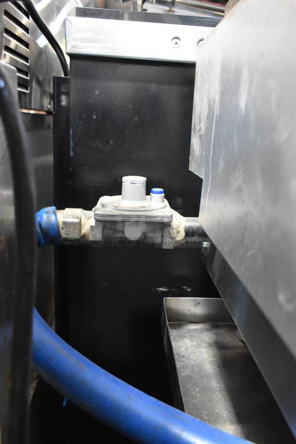 Stainless steel gas-powered flat top griddle by Standard Range on stand, showing gas connection detail.